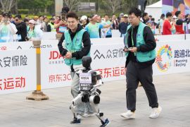 A robot and its engineers run in a marathon in Beijing, China, 19 April 2025. [Jessica Lee/EPA-EFE/]
