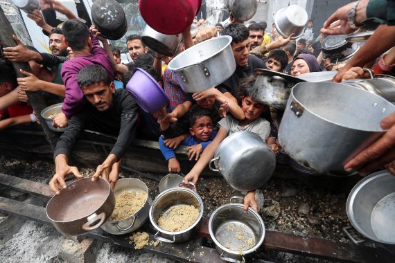 Palestinians wait to receive food cooked by a charity kitchen, in Jabalia,