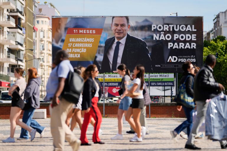 People walk past and election campaign billboard showing incumbent Prime Minister and leader of the center-right Social Democratic Party Luis Montenegro, in Lisbon, Monday, May 12, 2025, ahead of the May 18 general election. (AP Photo/Armando Franca)